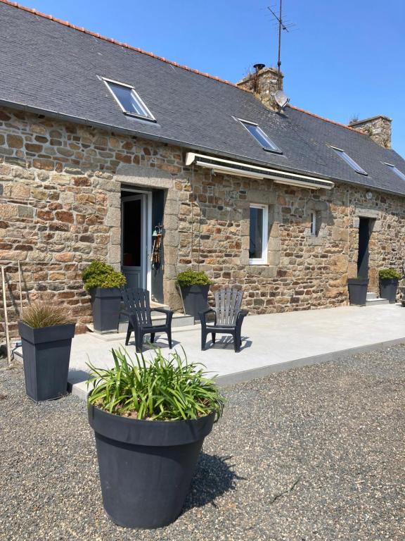 un bâtiment en pierre avec deux chaises et des plantes devant lui dans l'établissement La ferme de kervoas, à Lézardrieux