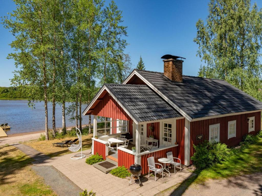 a red cottage with a table and chairs in front of the water at Holiday Home Sepelkyyhky by Interhome in Hirsjärvi