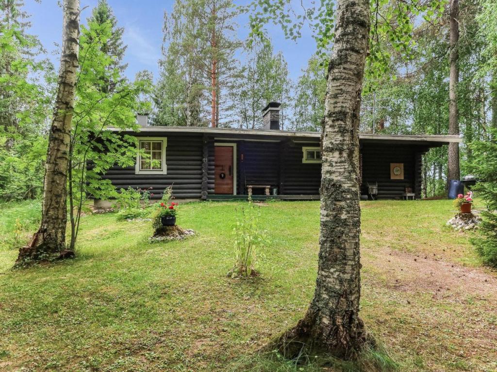 a black cabin in the woods with two trees at Holiday Home Revonkanta by Interhome in Kauhaniemi