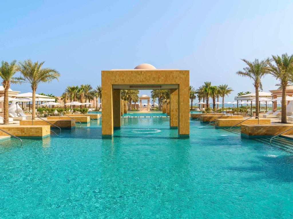 Rixos Marina Abu Dhabi في أبوظبي: مسبح في منتجع فيه ماء ازرق و نخيل