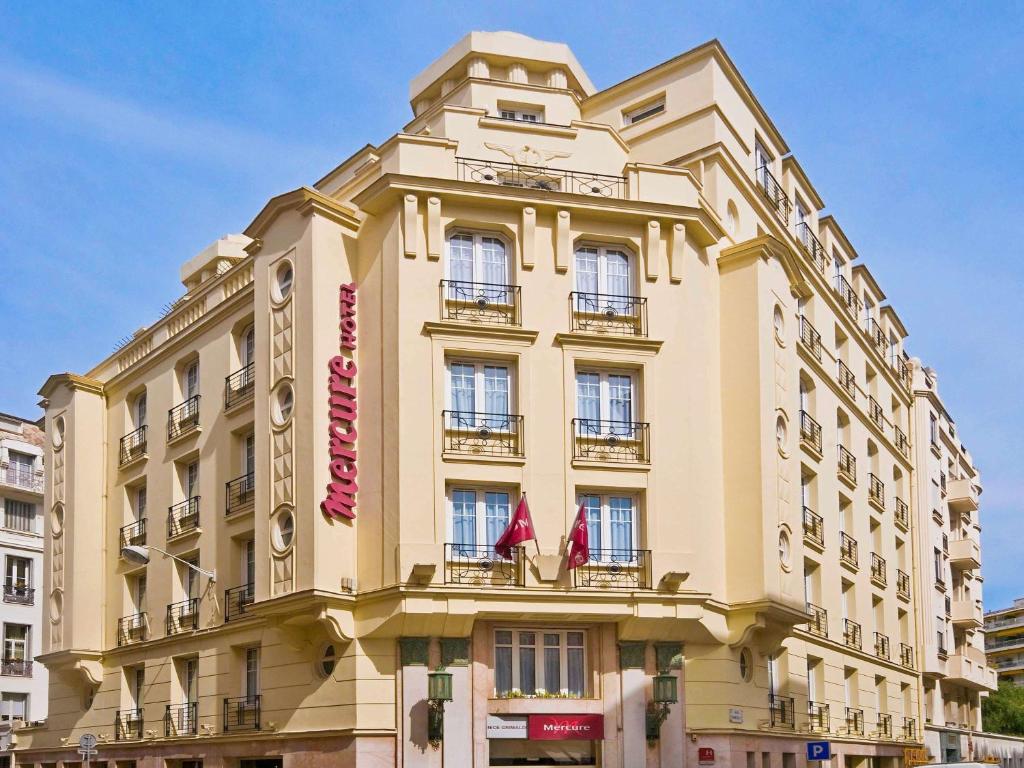 a large yellow building with red flags on it at Mercure Nice Centre Grimaldi in Nice