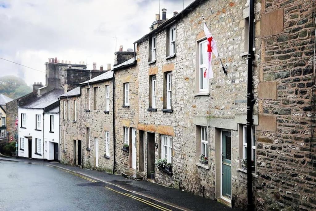 un viejo edificio de ladrillo con una bandera en una calle en Spinners Cottage - Central Kirkby Lonsdale Retreat, en Kirkby Lonsdale