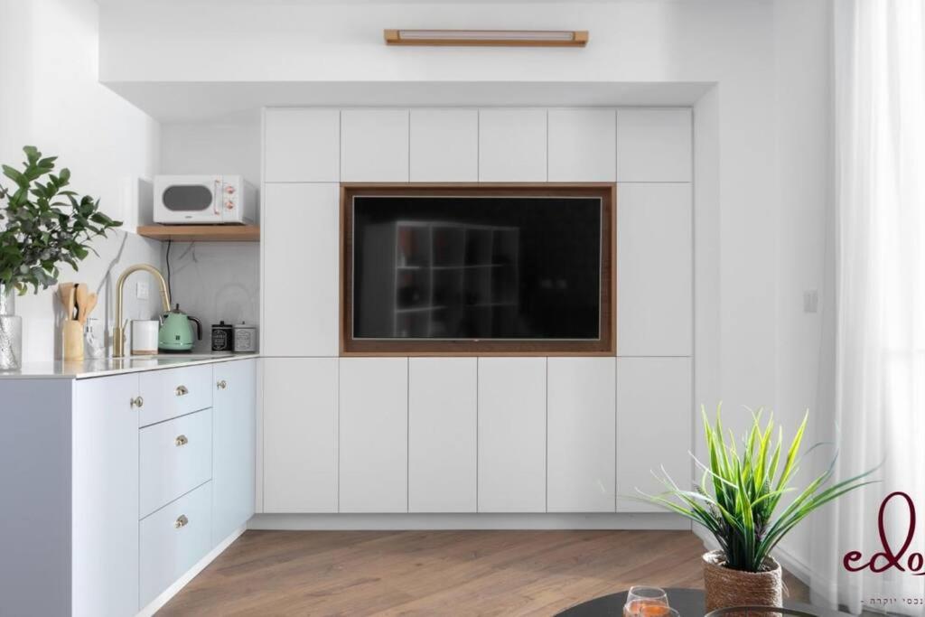 a kitchen with white cabinets and a tv on the wall at דירה במתחם סי סייד 50 מטר מהים - By Edomlux in Eilat