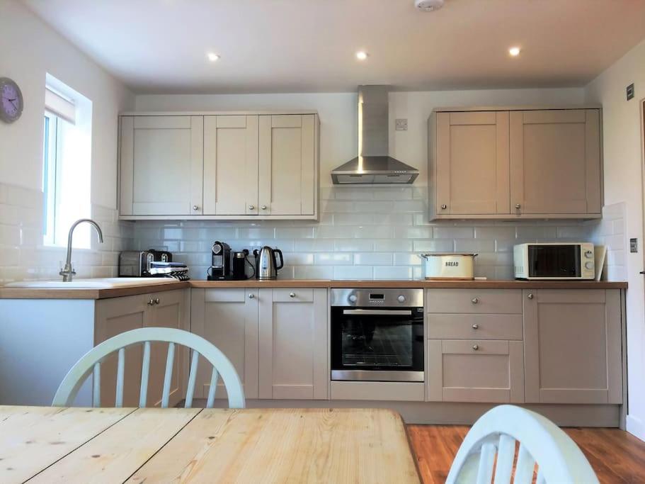 a kitchen with white cabinets and a wooden table at Chy Bownder Cottage in Lostwithiel