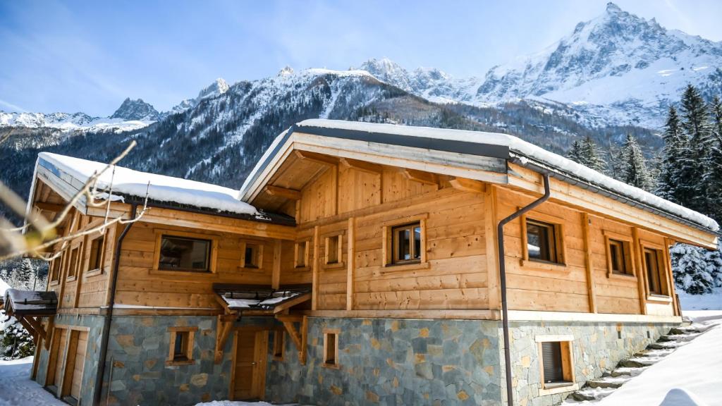 a log cabin in the snow with mountains in the background at Chalet Chal'heureux + Annexe in Chamonix-Mont-Blanc
