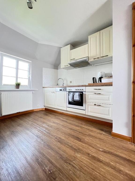 an empty kitchen with white cabinets and wooden floors at Strandperle in List