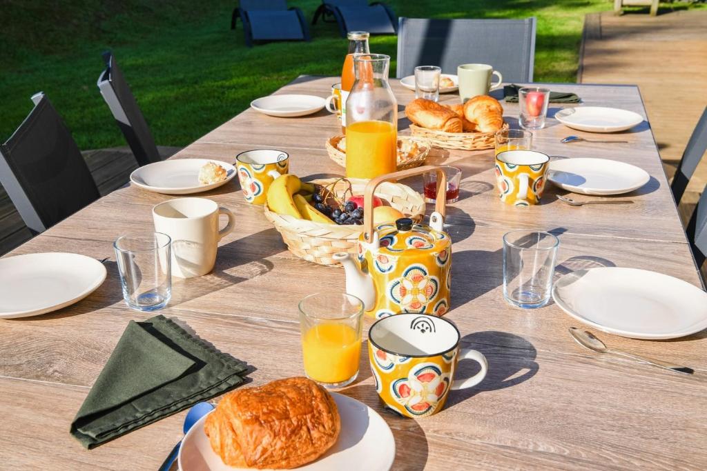 a wooden table with breakfast foods and orange juice at Maison Mélèry in Saint-Pierre-du-Val