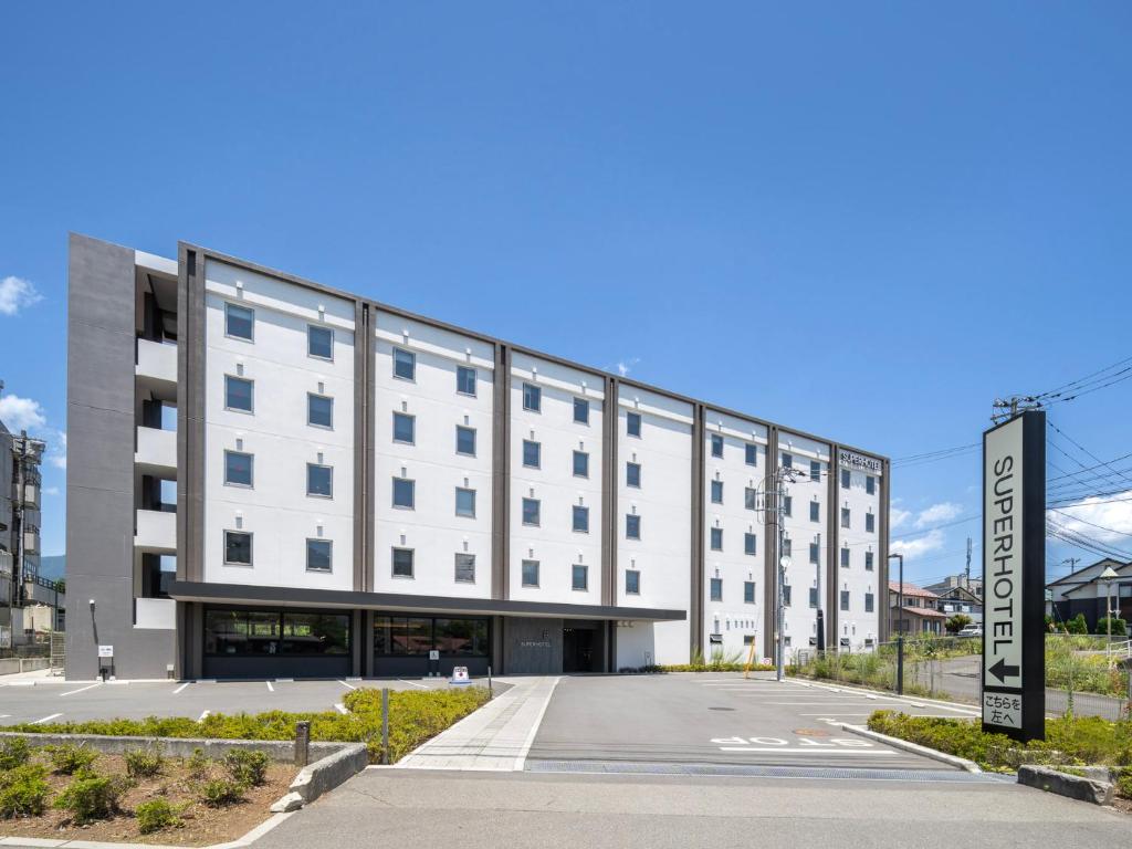 un grand bâtiment blanc avec un parking dans l'établissement Super Hotel Fujikawaguchiko Tennenonsen, à Fujikawaguchiko