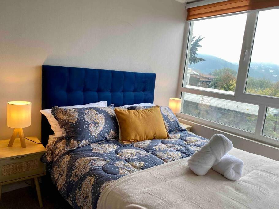 sypialnia z łóżkiem z niebieskim zagłówkiem i oknem w obiekcie Departamento A pasos del Centro de Temuco w mieście Temuco