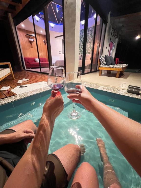 two people holding glasses of wine in a swimming pool at Macas Glamping in Macas