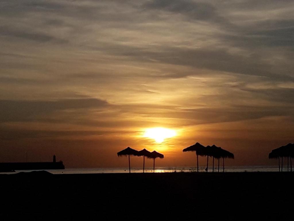 un grupo de sombrillas en una playa con puesta de sol en Apartamento Playa Blanca en Melilla