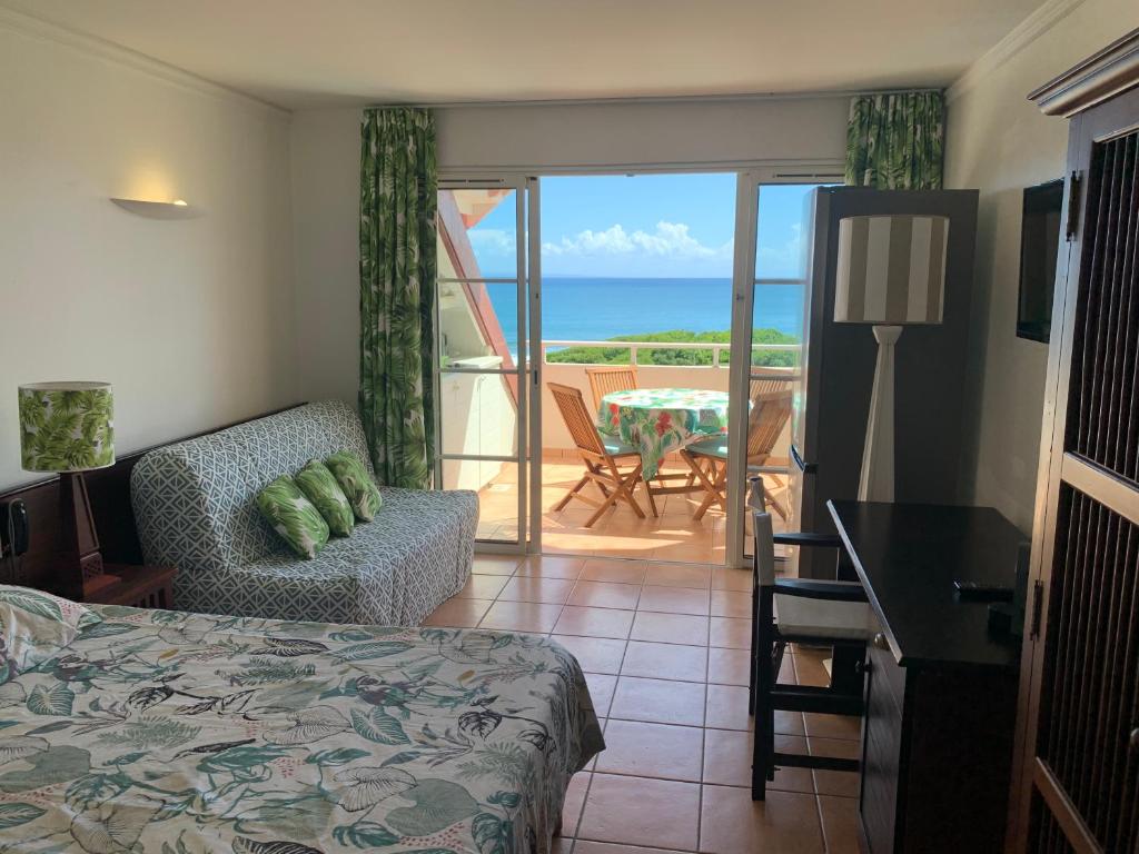 a bedroom with a bed and a balcony with the ocean at Studio Cannelle Vue Mer Village Vacances Sainte Anne in Sainte-Anne
