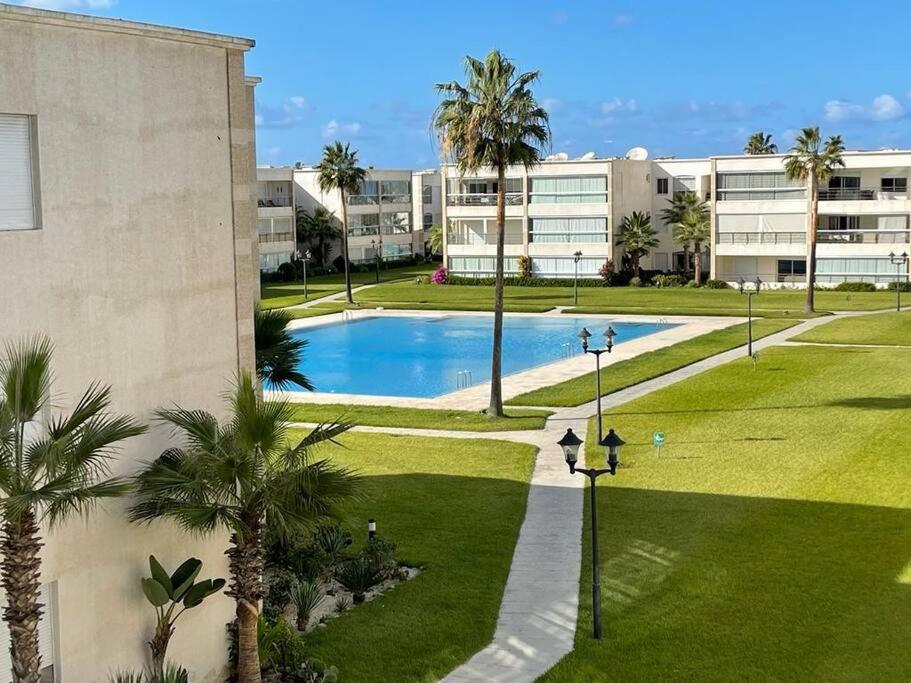 una piscina en un parque con palmeras y edificios en appartement chic et ensoleillé ola blanca 2, en Dar Hamida