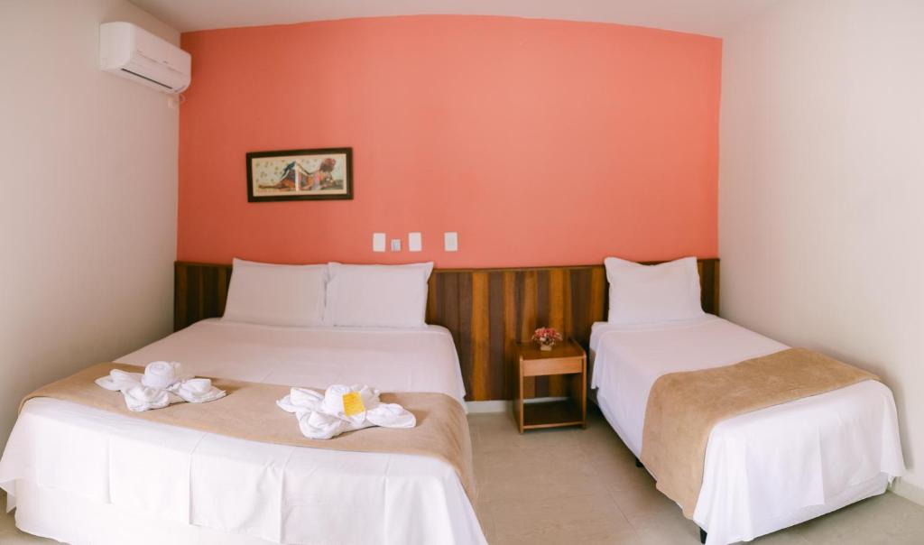 2 Betten in einem Zimmer mit orangefarbenen Wänden in der Unterkunft Hotel Kiribati Maresias in Maresias