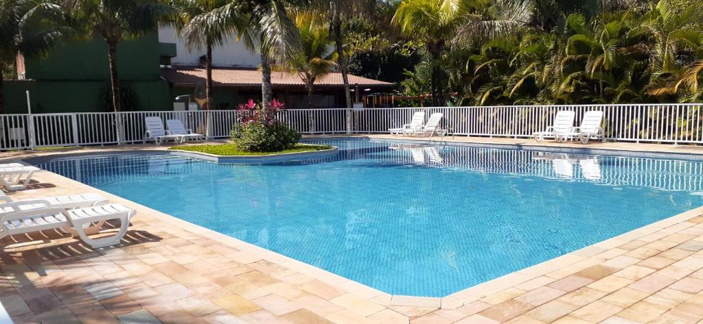 a large swimming pool with chairs and palm trees at Excelente casa em condomínio fechado em Juquehy. 2 suítes, ar, piscina comum. in São Sebastião