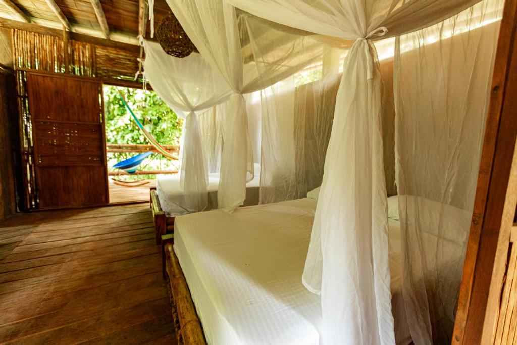 1 dormitorio con cama con dosel y cortinas blancas en La Martina Ecolodge, en Nuquí