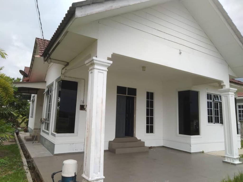 een wit huis met een veranda en zuilen bij Familia Homestay Tepi Sawah in Pasir Mas