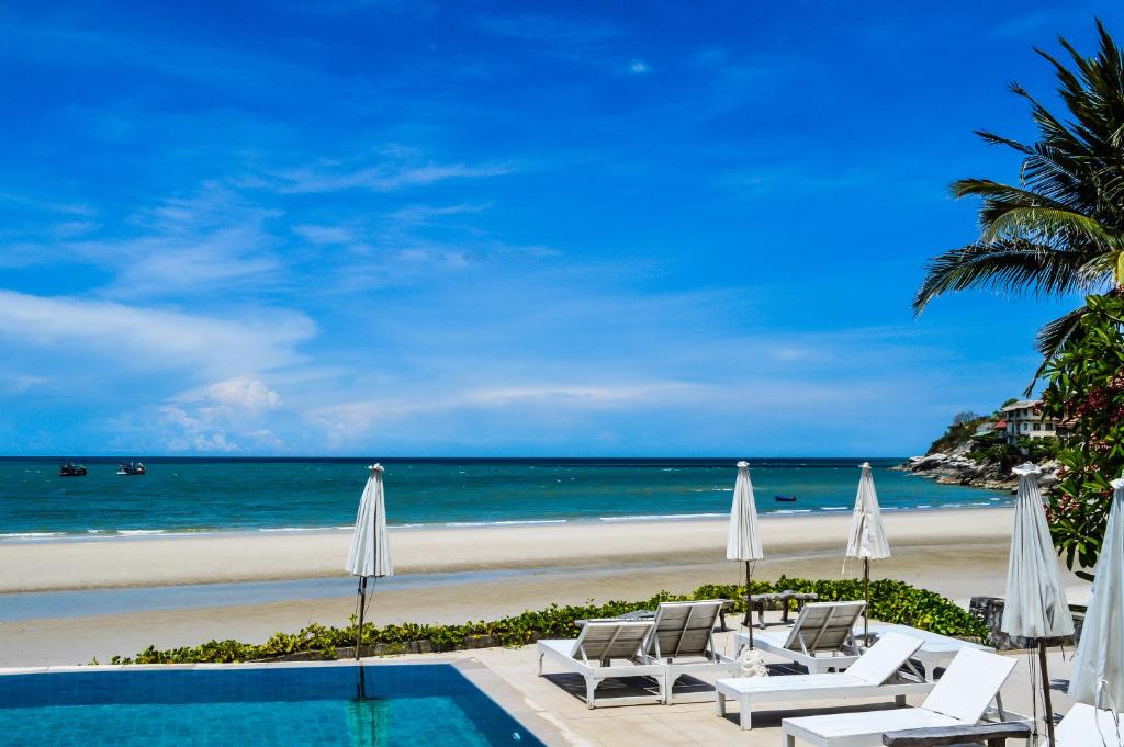 a pool with chairs and umbrellas next to a beach at Nern Chalet Beachfront Hotel in Hua Hin