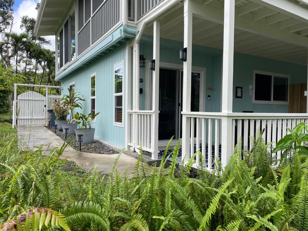 a blue house with a white porch and plants at Hale O Malu at Kaloli Point in Keaau