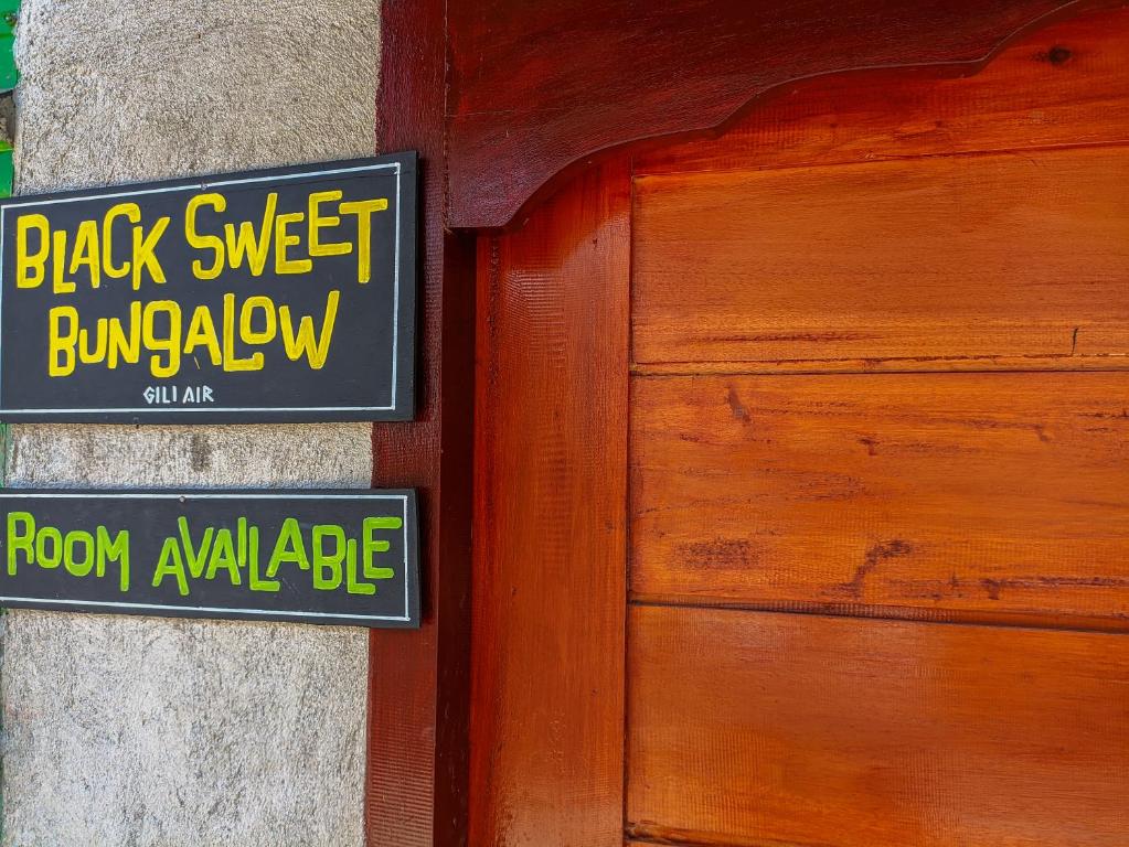 a black and yellow sign next to a wooden door at BLACK SWEET BUNGALOW in Gili Air