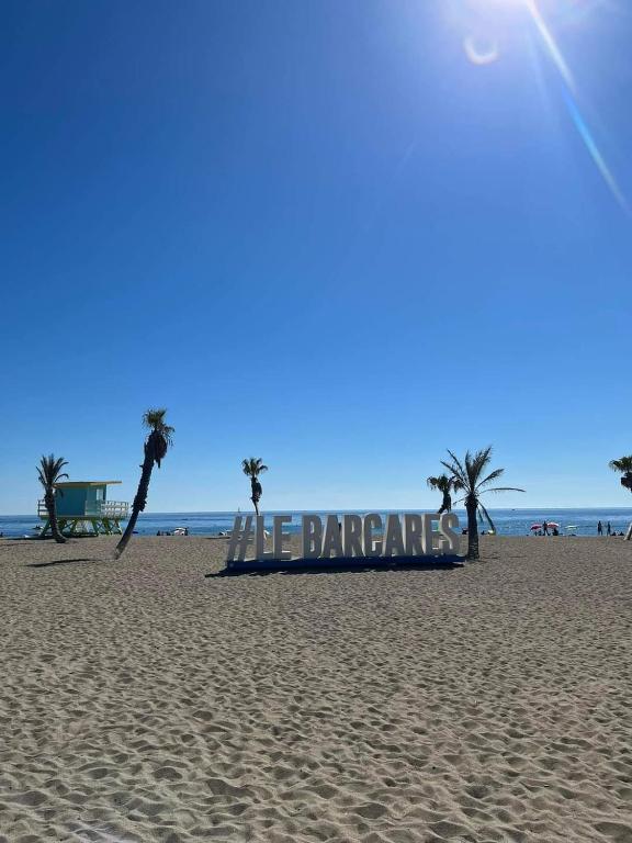 un panneau sur une plage avec des palmiers et l'océan dans l'établissement Le Barcarès secteur Lydia, au Barcarès
