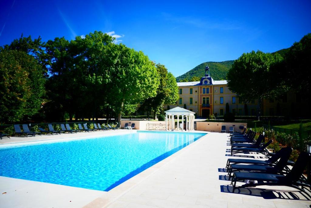 une piscine avec des chaises longues et un bâtiment dans l'établissement La Vue est Belle, à Montbrun-les-Bains