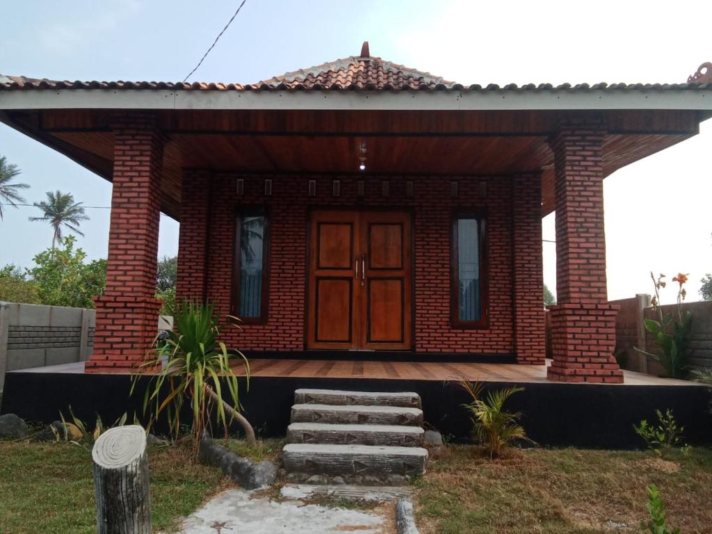 uma pequena casa de tijolos vermelhos com uma porta de madeira em Rumah Pantai Krui em Wainapal