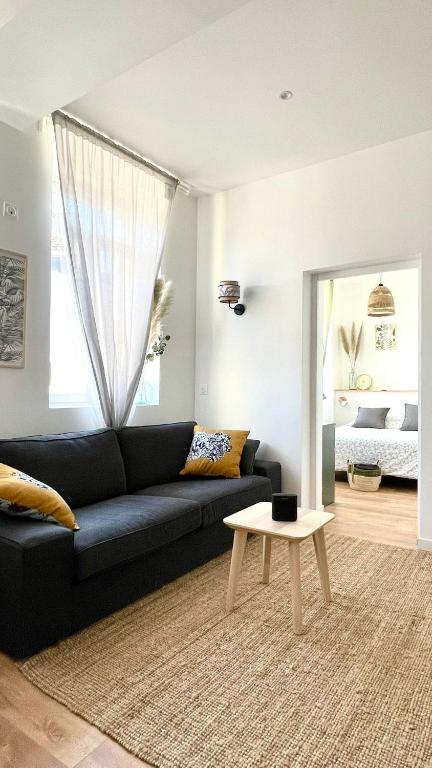 a living room with a black couch and a table at Chez Clement et Mathilde - T2 hyper centre tout équipé in Saint-Amand-les-Eaux