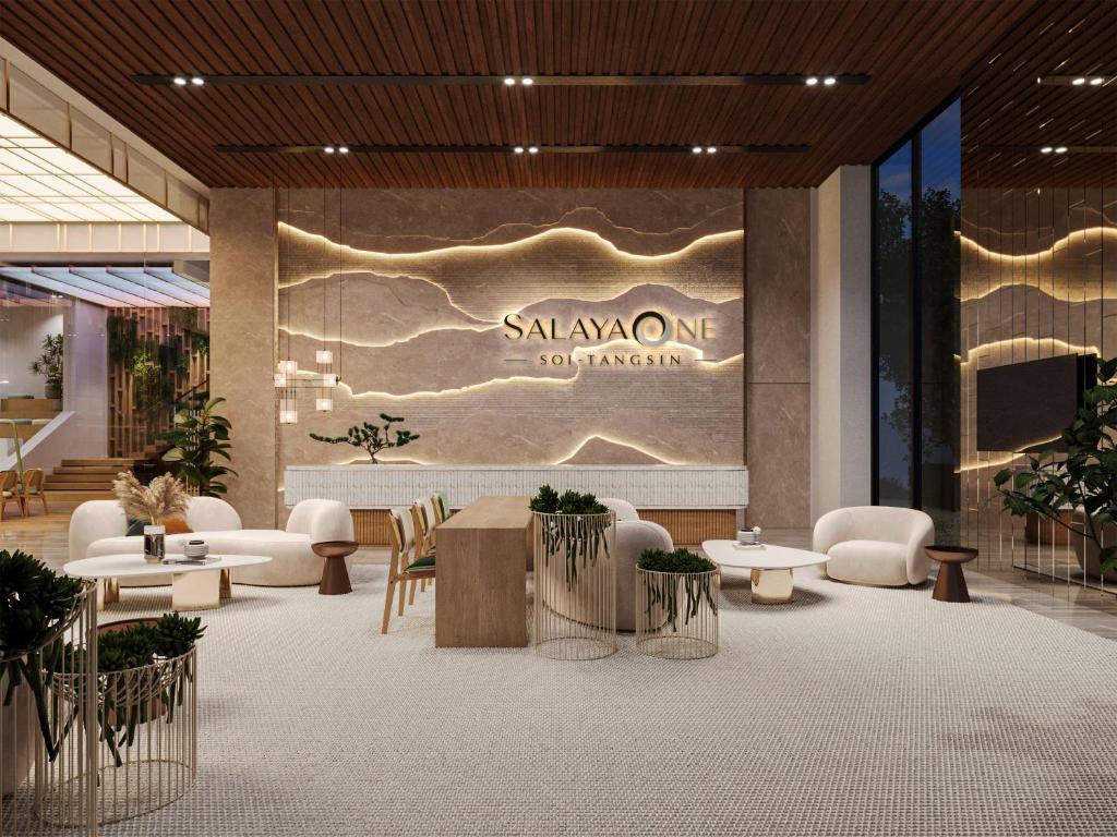 a lobby with tables and chairs and a sign on a wall at Salaya One Hotel & Service Apartment in Salaya