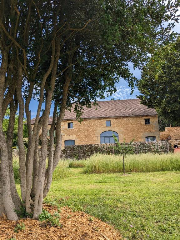 une grande maison en briques avec des arbres devant elle dans l'établissement La Grange Symphorine, chambre d'hôtes de charme située entre la vallée de la Dordogne et la vallée de la Vézère, à Meyrals