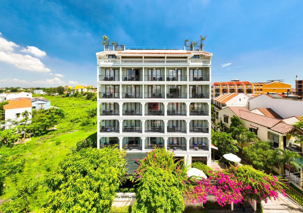 a tall white building with flowers in front of it at Cozy Savvy Boutique Hotel Hoi An in Hoi An