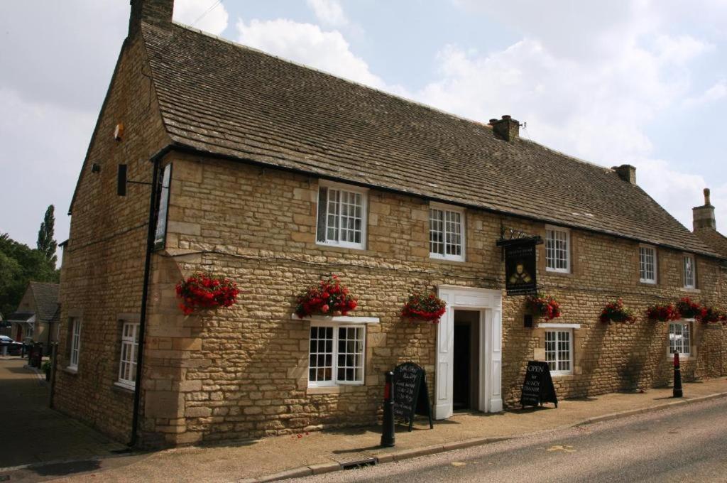 um antigo edifício de tijolos com flores nas janelas em Queen's Head Inn em Nassington