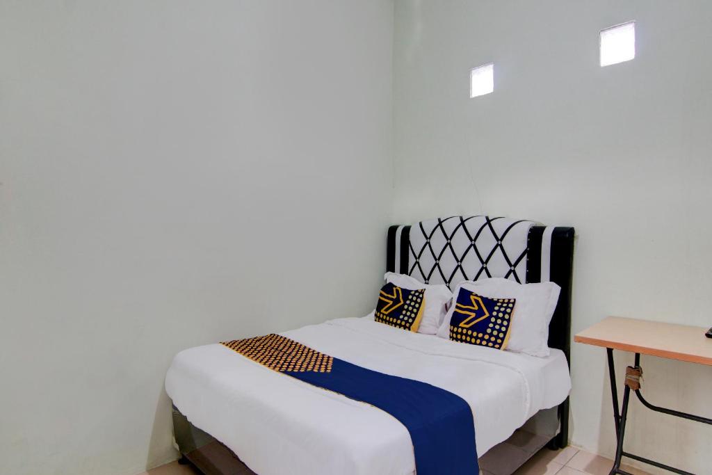 Una cama blanca con almohadas azules y amarillas. en SPOT ON 92797 Awi Stay Syariah, en Dumai