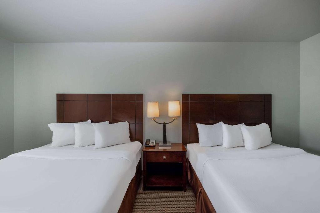 two beds in a hotel room with white sheets at Baymont by Wyndham Rapid City in Rapid City