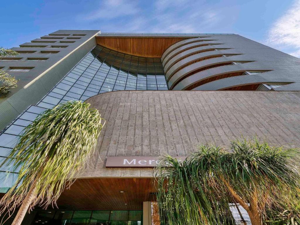 a large building with palm trees in front of it at Mercure Belo Horizonte Vila da Serra in Belo Horizonte