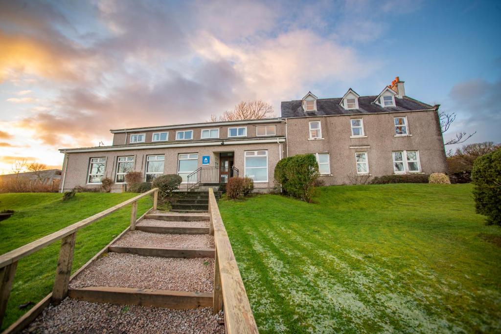 a large house on a green field with a wooden fence at Broadford Youth Hostel in Broadford