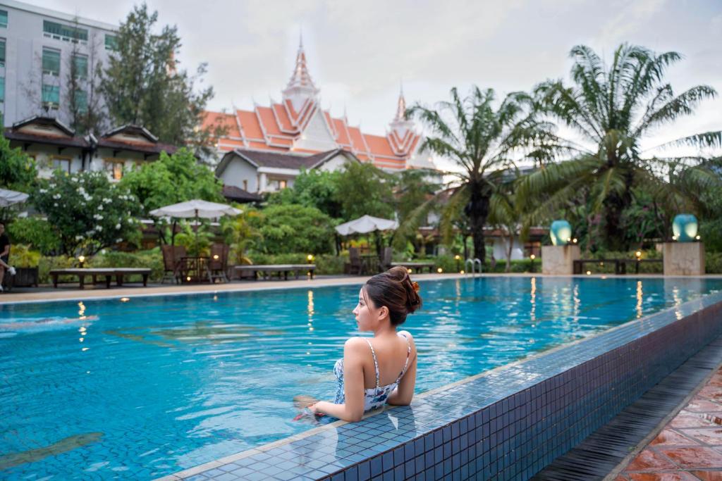 una mujer sentada en una piscina en un resort en Les Jardins Du Bassac en Phnom Penh