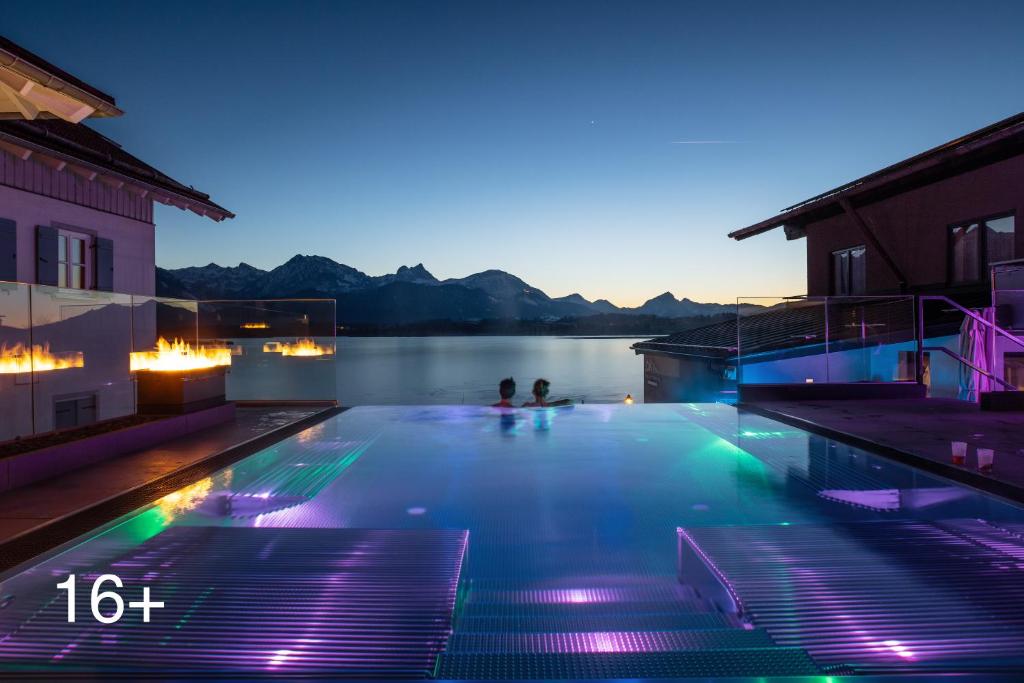 a swimming pool with lights in the water at night at Hotel am Hopfensee in Füssen