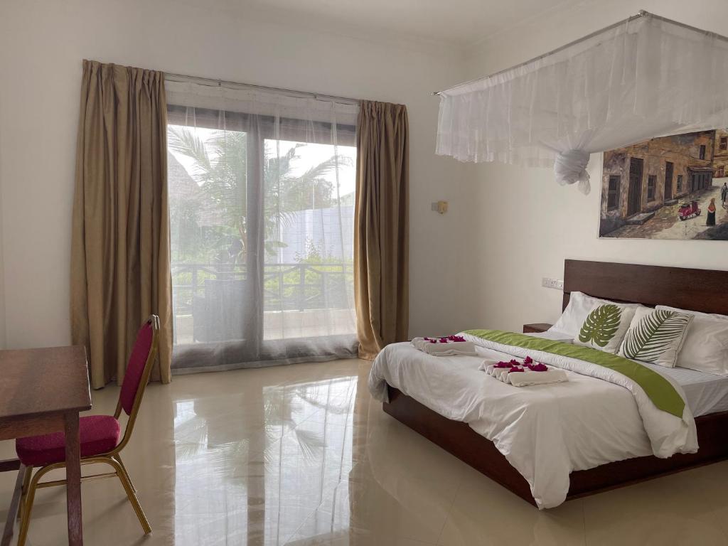 een slaapkamer met een bed, een tafel en een raam bij Minah Bungalows in Nungwi