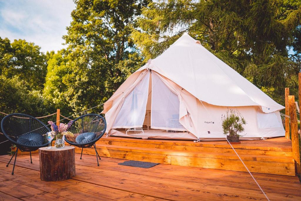 - une tente blanche sur une terrasse en bois avec des chaises dans l'établissement Glamping U hranic, à Červená Voda