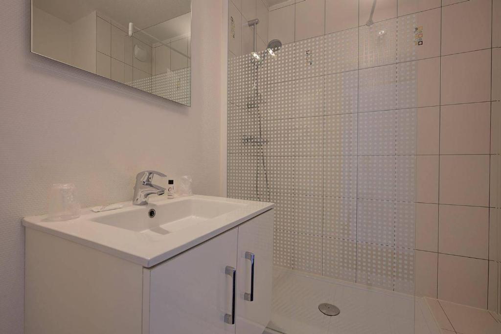 a white bathroom with a sink and a shower at Hôtel Le Nautic in Arcachon