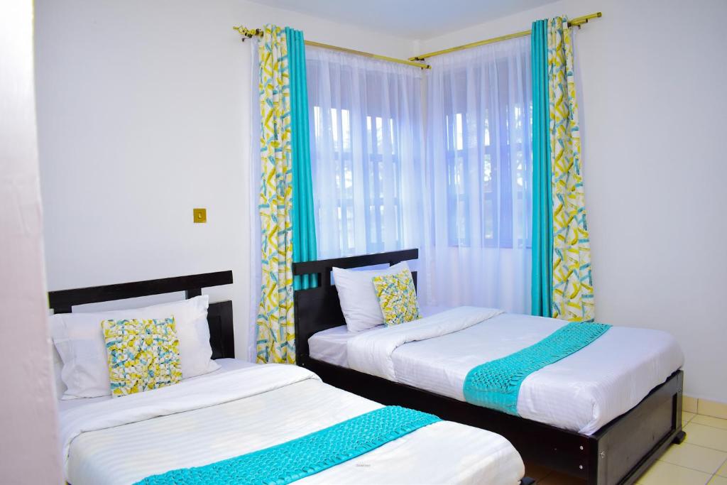 two beds in a room with blue curtains at Bomani Penthouse in Kisumu