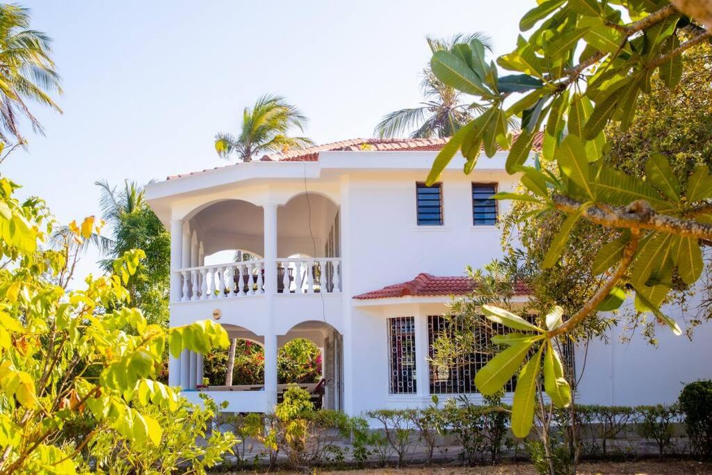 a white house with a balcony and trees at Sand and Shells Beach House- 4 Bedroom with a pool in Mombasa