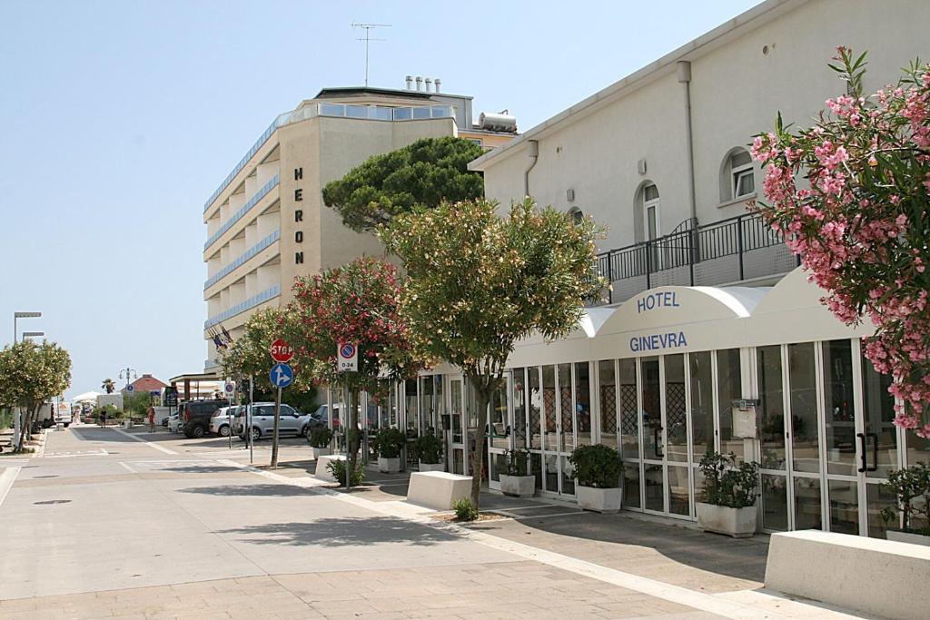 eine Straße mit einem Gebäude, Bäumen und Blumen in der Unterkunft Hotel Ginevra in Lido di Jesolo