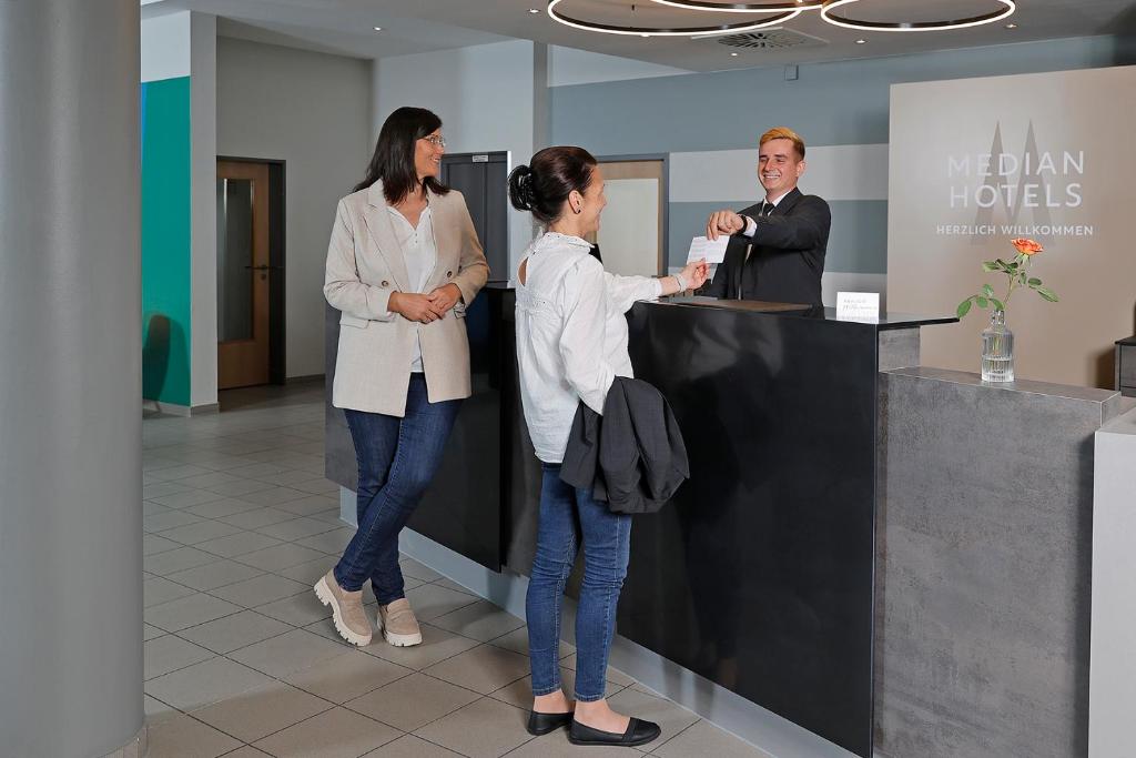 3 Personen stehen an einer Theke in einer Lobby in der Unterkunft Median Hotel Hannover Messe in Hannover