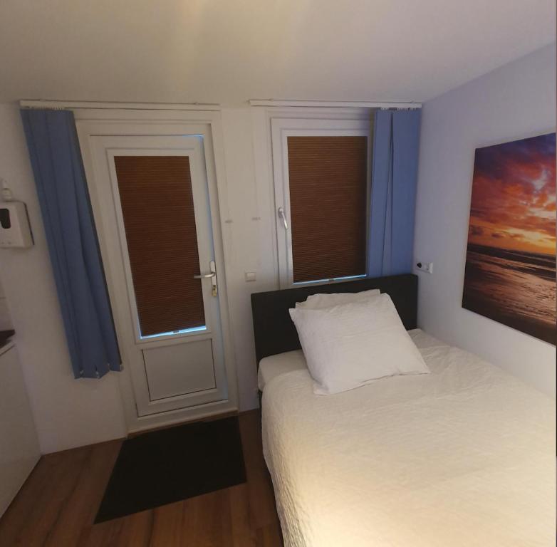 a bedroom with a bed and two windows with blue curtains at Cozy Garden House kijkduin Beach in The Hague