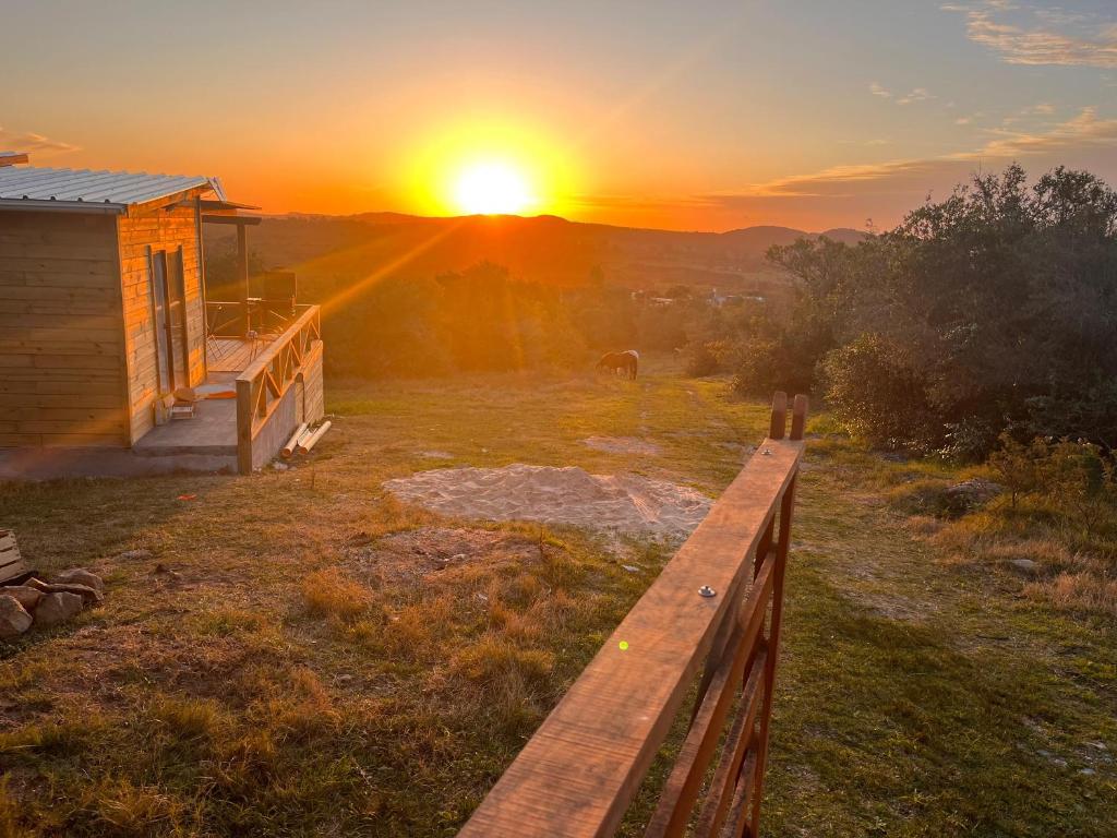 um pôr-do-sol sobre um campo com uma cerca e uma casa em Cabaña Los Ceibos. em Villa Serrana