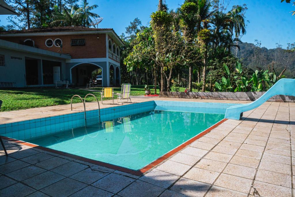 a swimming pool with a slide in front of a house at Recanto Dom José in Peruíbe