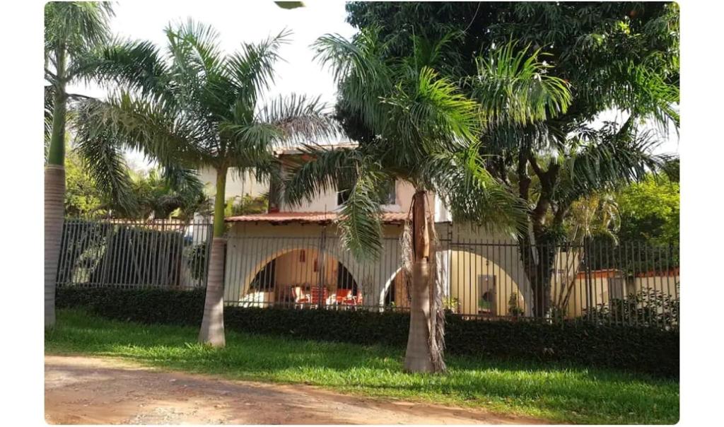 ein Haus mit Palmen vor einem Zaun in der Unterkunft Casa de 4 habitaciones con piscina en barrio cerrado a 5 minutos del Aeropuerto Internacional in Luque