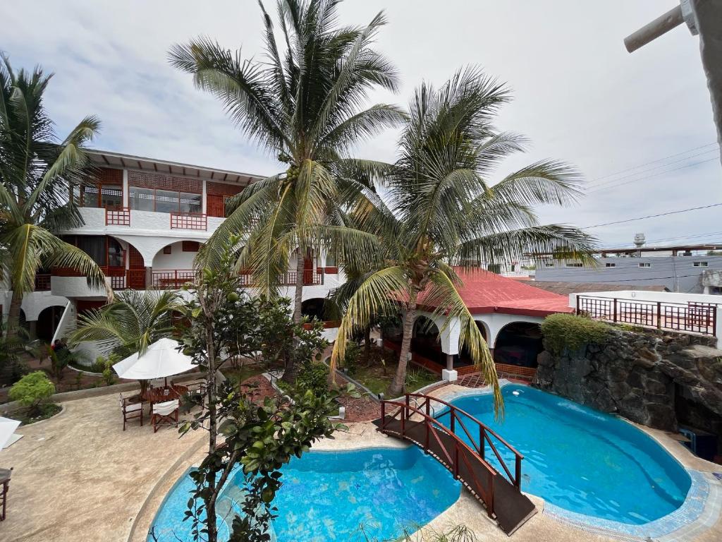 un complexe avec une piscine, des palmiers et un bâtiment dans l'établissement Hotel Silberstein, à Puerto Ayora